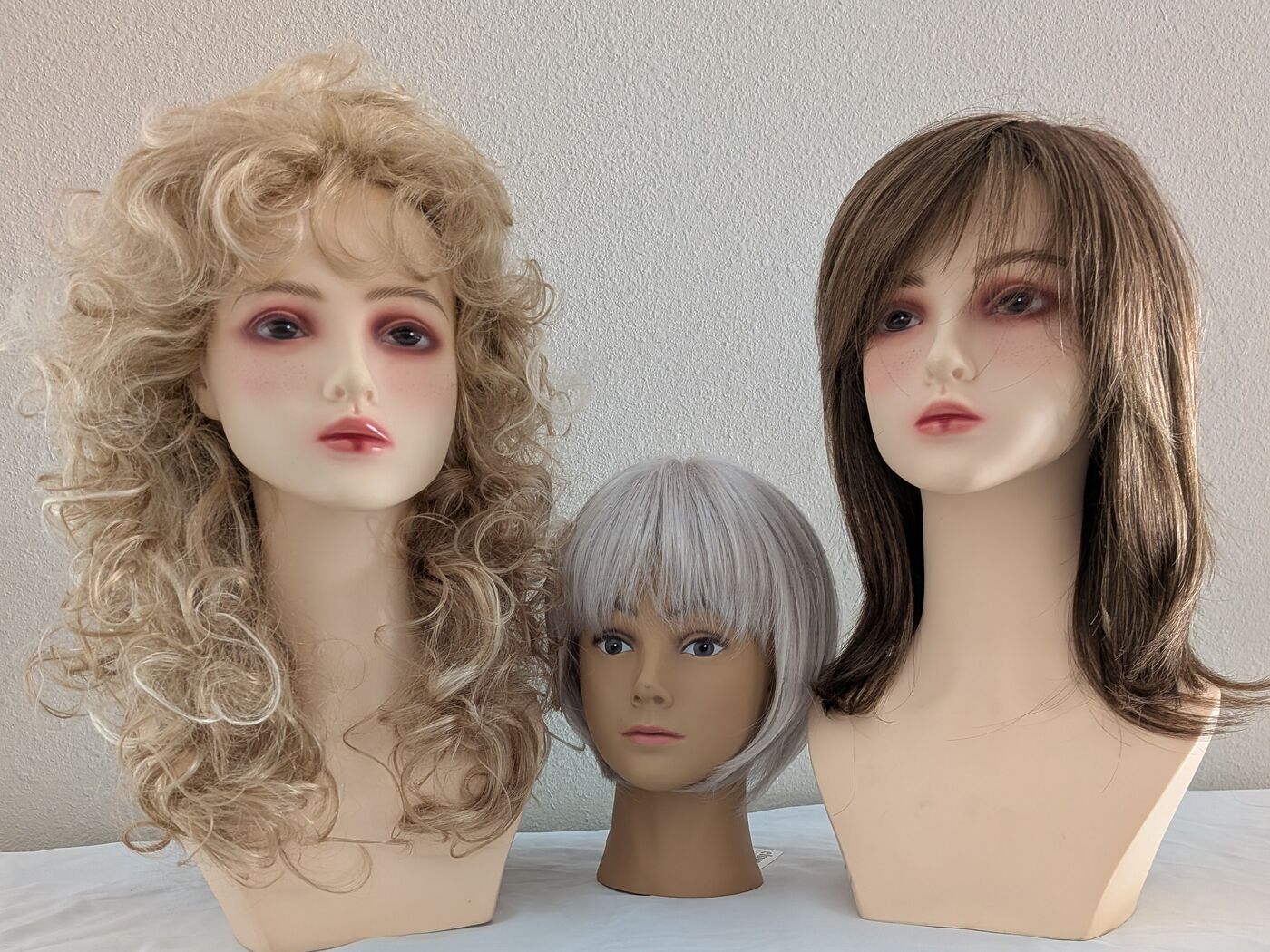 A full curly blonde wig, a soft silver pixie cut, and a straight brunette style with bangs.